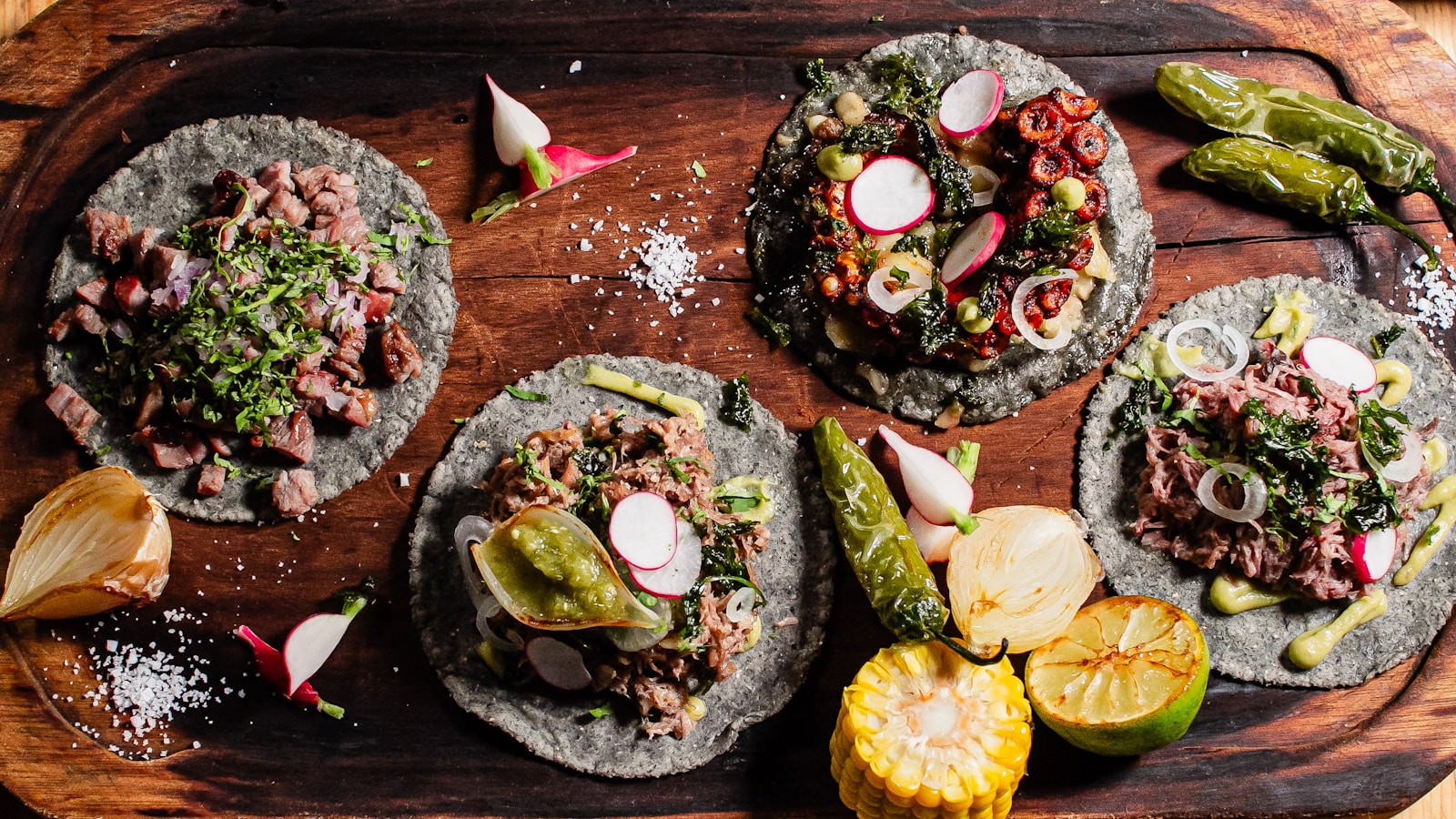 Four gourmet tacos with assorted toppings on wooden board